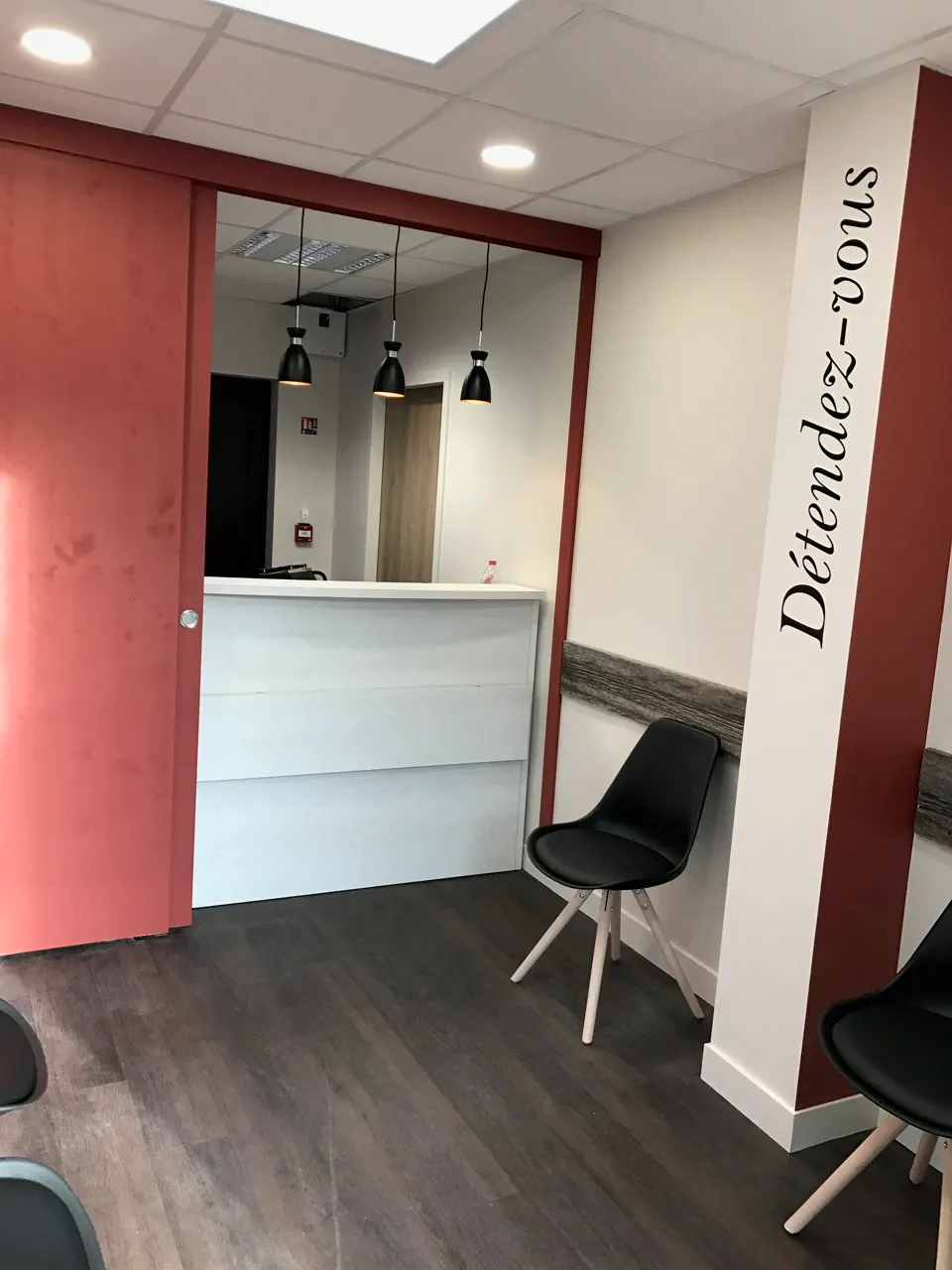 Banque d'accueil blanche devant un mur rouge, avec deux chaises noires et un panneau vertical portant l'inscription « Détendez-vous ».