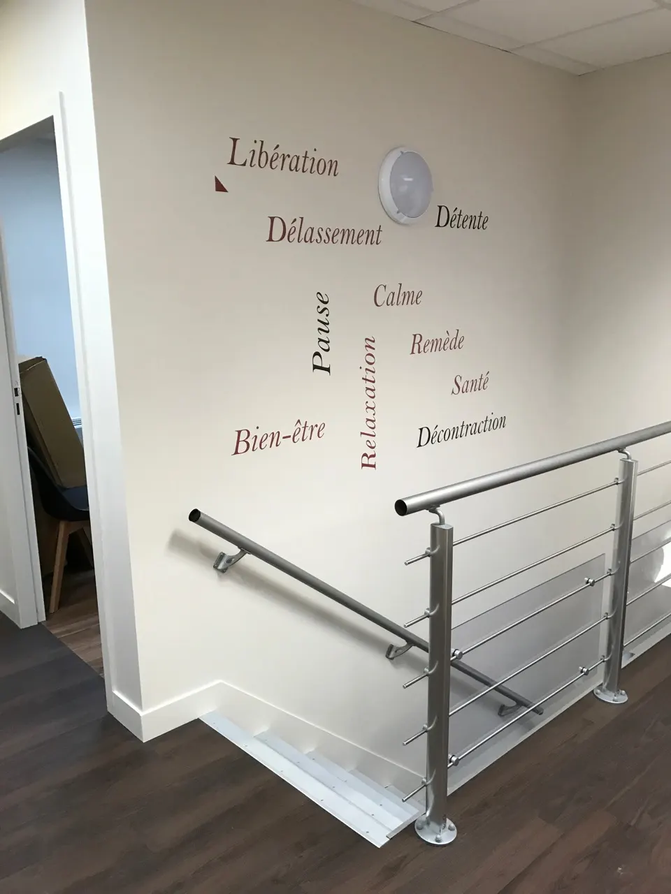 Trémie d'escalier bordée d'un garde-corps en acier inoxydable à lisses horizontales, devant un mur clair orné de mots en lettres adhésives.