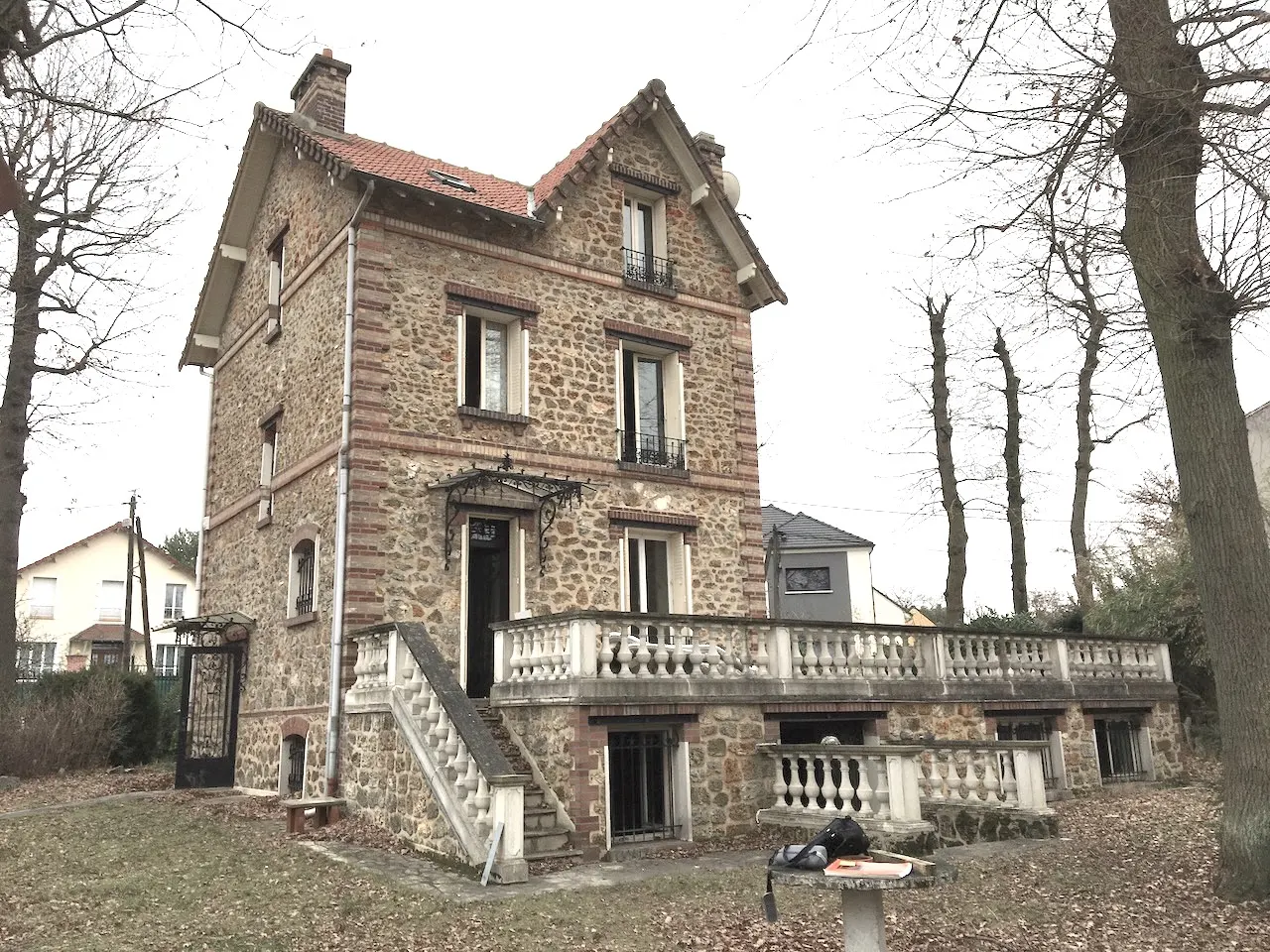 La même maison en meulière vue depuis le jardin en hiver, arbres sans feuilles.
