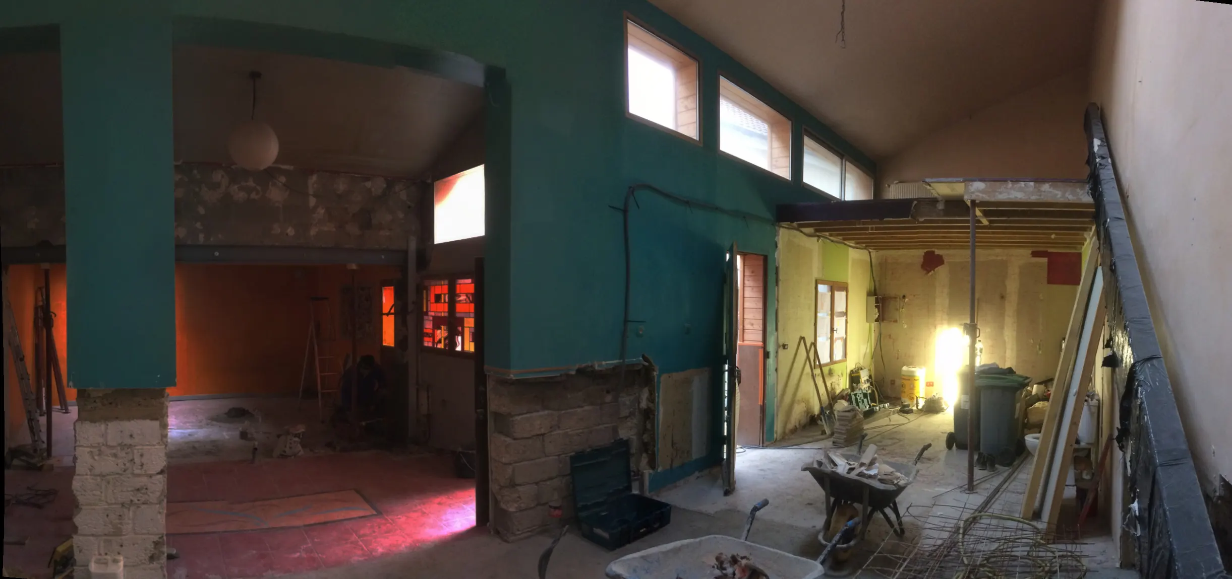 Vue panoramique d'un intérieur en chantier : sols décapés, murs mis à nu, outillage et gravats au sol.