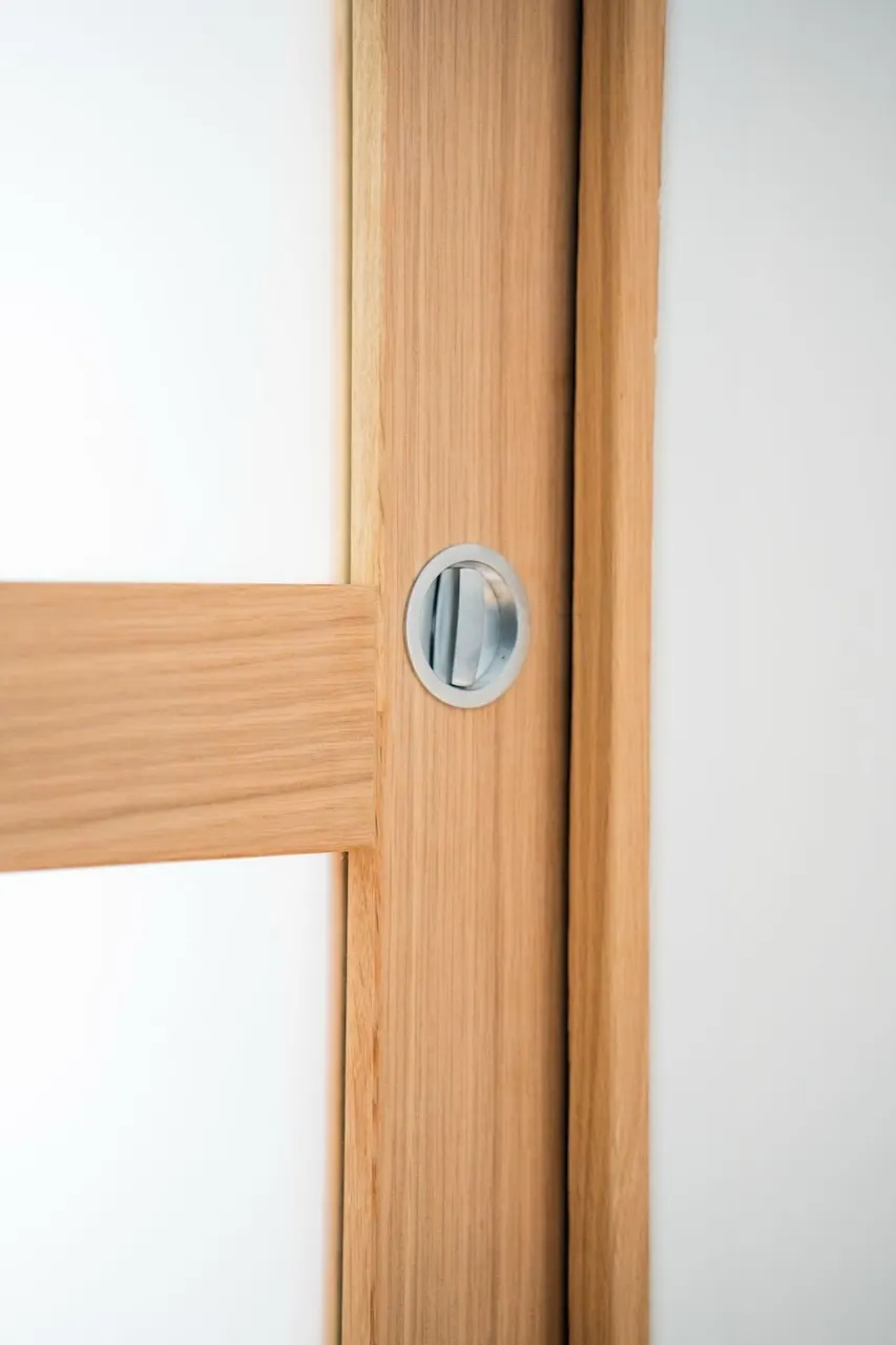 Gros plan sur une porte en bois clair avec une poignée ronde encastrée en métal.